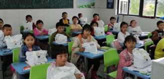 Classe de l'école primaire Wangjian en Chine avec des enfants assis devant leur bureau avec des kits sanitaires