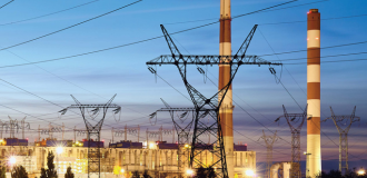 Night view of power generation plants illuminated, featuring electricity towers against a dark sky.