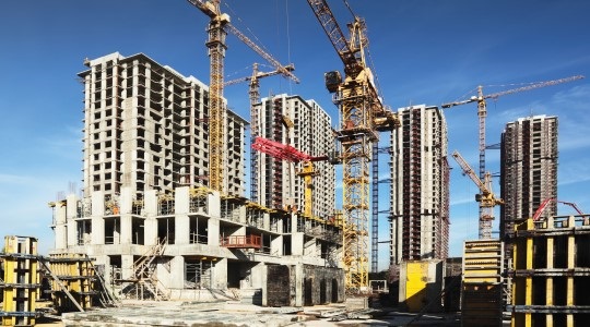 Construction site featuring cranes and buildings in various stages of development against a clear blue sky.