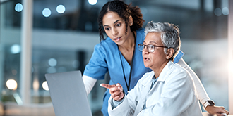 A nurse and a doctor reviewing a medical report on a hospital laptop.