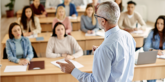 A professor giving a lecture to large group of college students in the classroom.