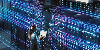 A chief technology officer using a laptop in a large data center room. 