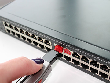 A network switch with two ports blocked by block-out devices, with a hand using a tool to remove one of the devices