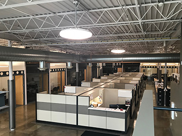 Interior view of an office area including a bank of cubicles, with glass-front offices around the exterior